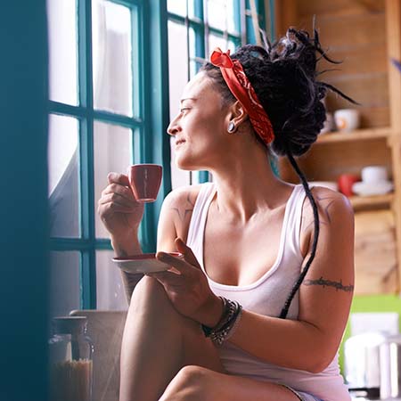 L'immagine mostra una signora che sorseggia un caffè guardando fuori dalla finestra
