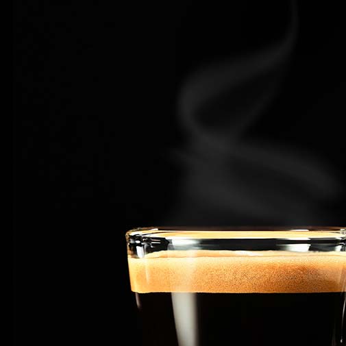 L'immagine mostra una tazzina di caffè fumante con uno sfondo scuro.